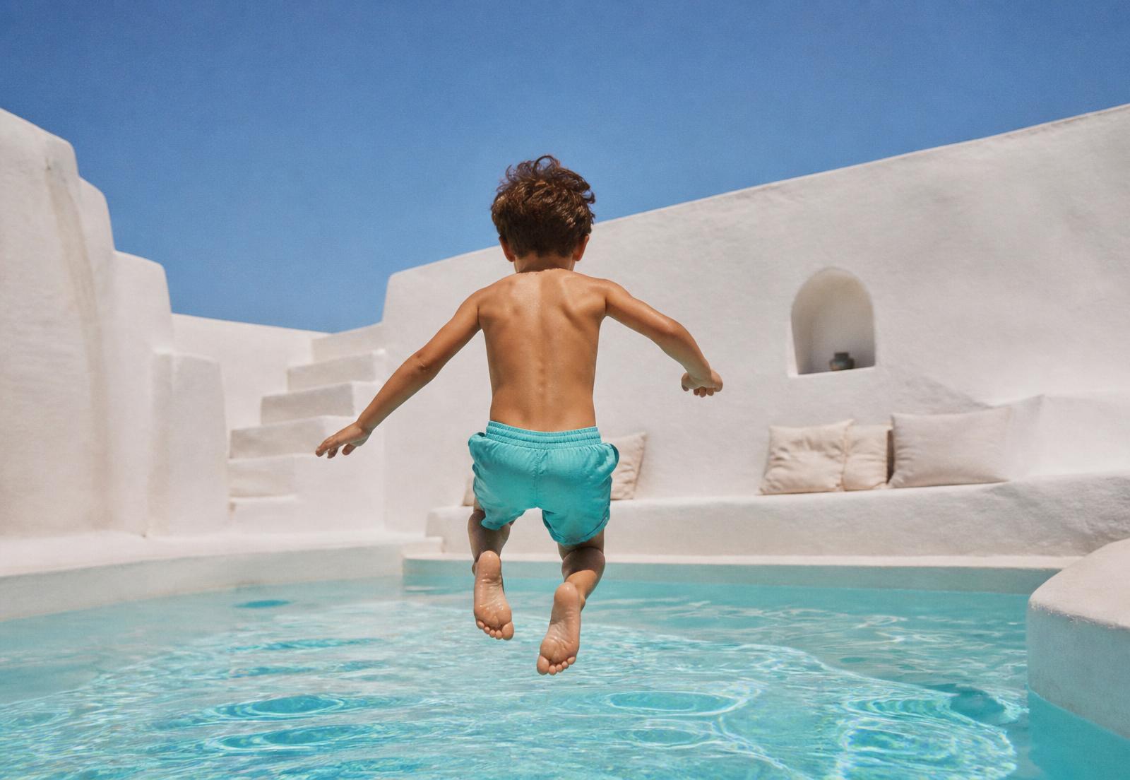 Niño saltando de espaldas a una piscina en una casa blanca mediterránea